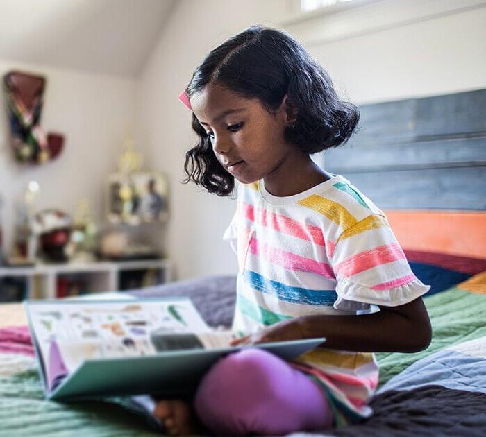 A young girl is sitting on a bed reading a book